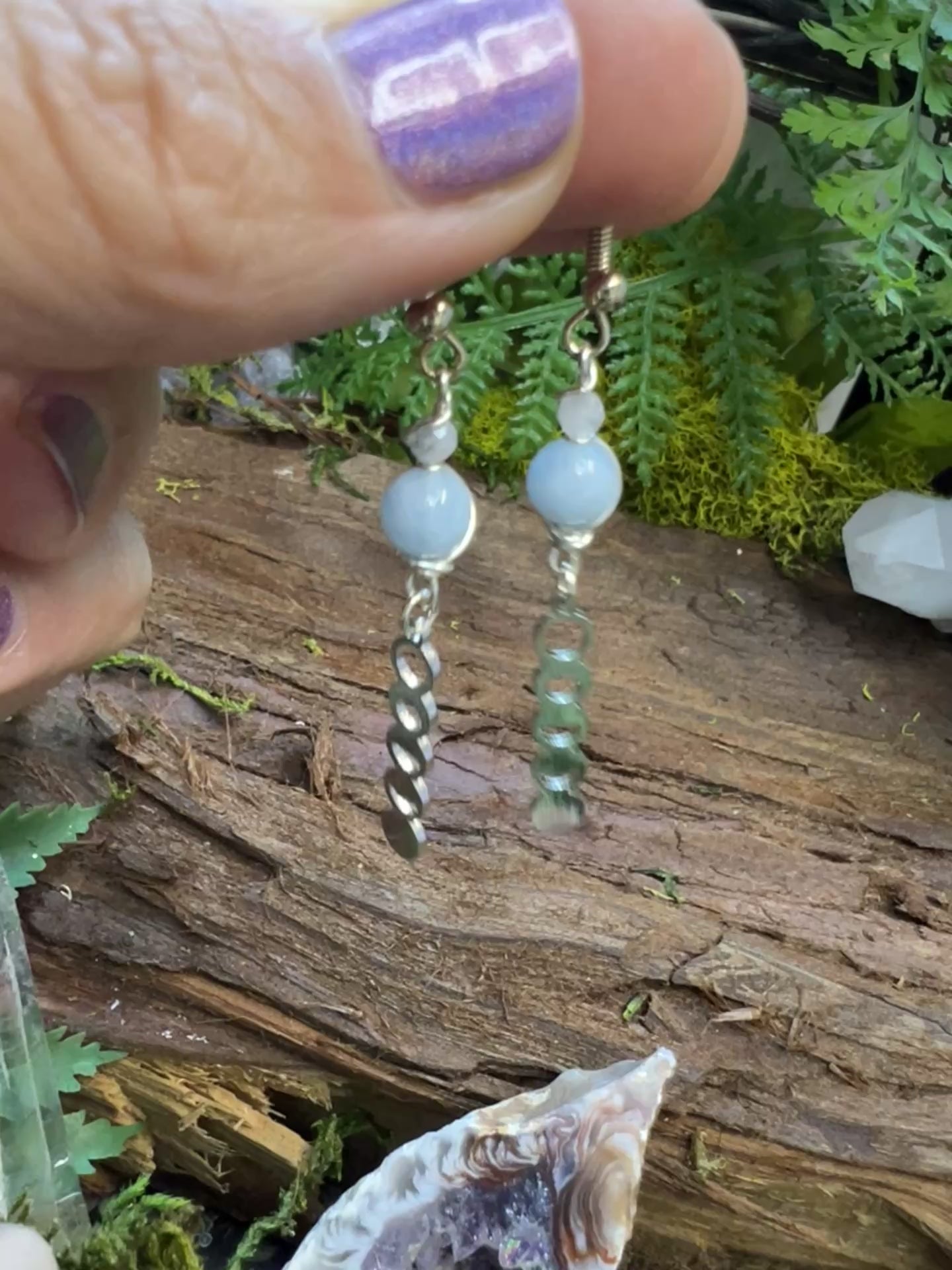 Serene aquamarine and moonstone earrings surrounded by greenery and crystal accents