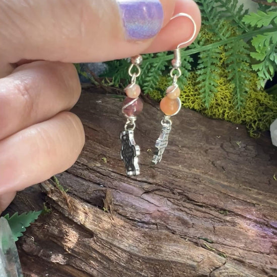 Spiritual pink jade earrings with stainless steel charms styled on natural wood with greenery