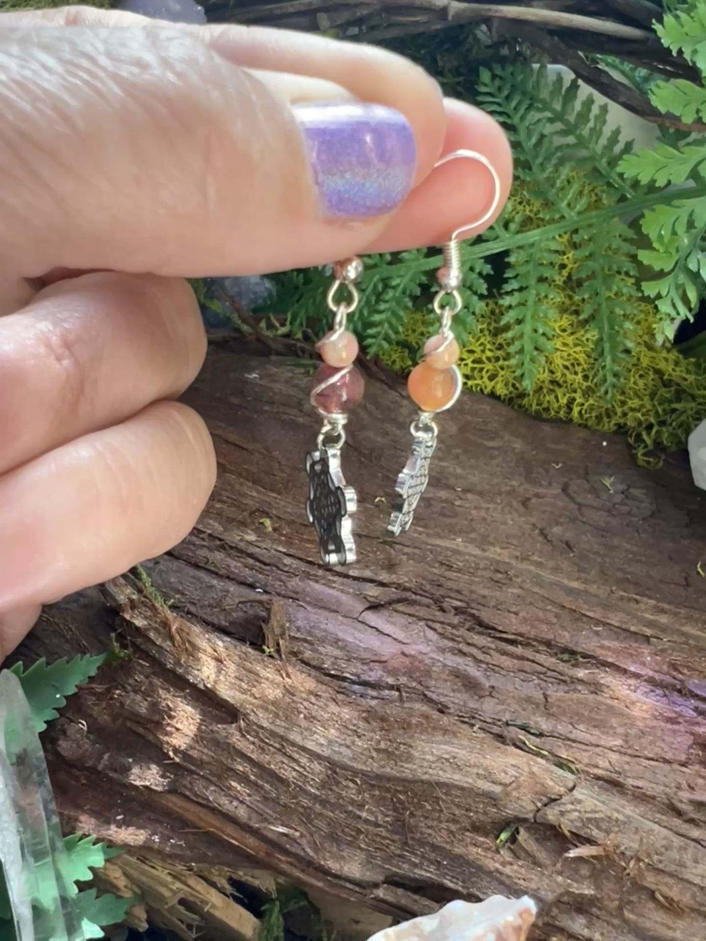 Spiritual pink jade earrings with stainless steel charms styled on natural wood with greenery