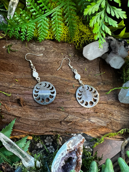 Rainbow moonstone lunar phase earrings held above wood and moss with crystals