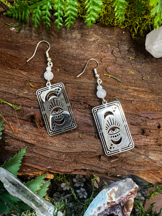 Rainbow moonstone tarot card earrings with moon and eye charms styled on mossy wood
