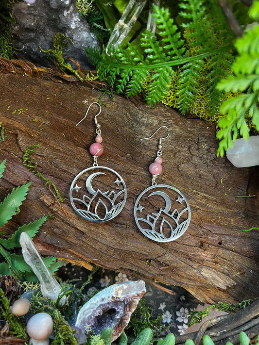 Rhodonite moon and lotus earrings styled on wood with moss and crystal accents