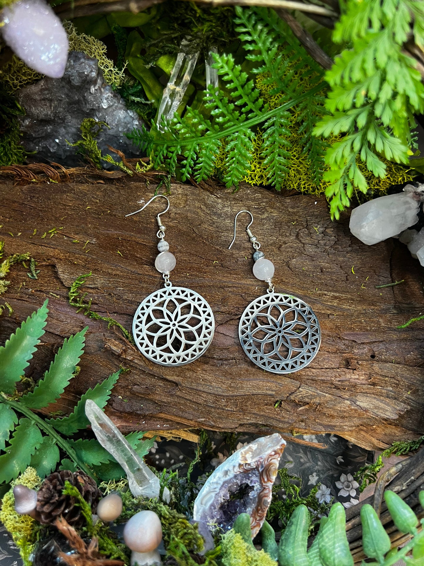 Silver mandala rose quartz and zebra jasper earrings on a wooden surface with greenery and crystals.