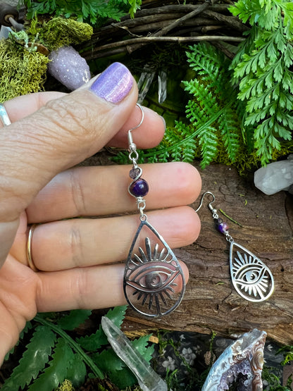 Protective crystal earrings with all-seeing eye charms on rustic forest backdrop
